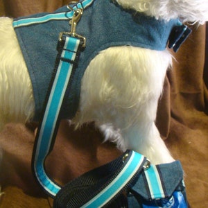 May include: Denim dog harness and lead set with light blue and white striped detailing. The harness has a metal clasp and a matching lead. A small bag dispenser is also included.