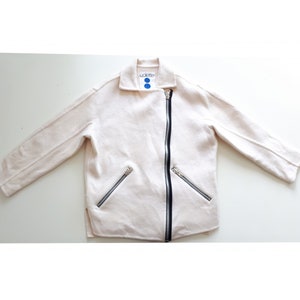 May include: A cream-colored zippered jacket with a black zipper and two zippered pockets. The jacket has a label that says "Violette" with two blue dots.