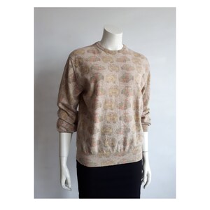 Puede incluir: Un suéter beige con un estampado floral multicolor. El suéter tiene mangas largas y cuello redondo.