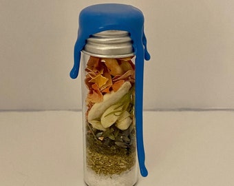 May include: A clear glass vial with a silver screw-top lid sealed with blue wax that drips down the side. The vial is filled with layers of dried botanical elements, including orange petals, white seeds, green herbs, and white granular salt.