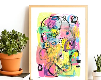 Op de afbeelding: Abstracte kunstafdruk in een licht houten frame. Het kunstwerk toont een levendige mix van kleuren, waaronder geel, roze, blauw en zwart. De compositie bevat verschillende vormen en lijnen, wat een dynamisch gevoel creëert. Een potplant en boeken staan op de achtergrond.