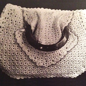 May include: A crocheted handbag with a black handle. The bag is made with a delicate, open stitch pattern.