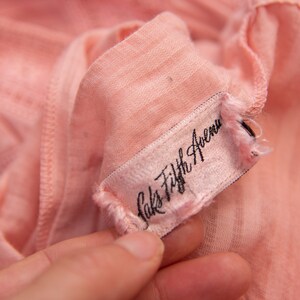 May include: A close-up of a pink fabric garment tag with black text that reads "Saks Fifth Avenue".