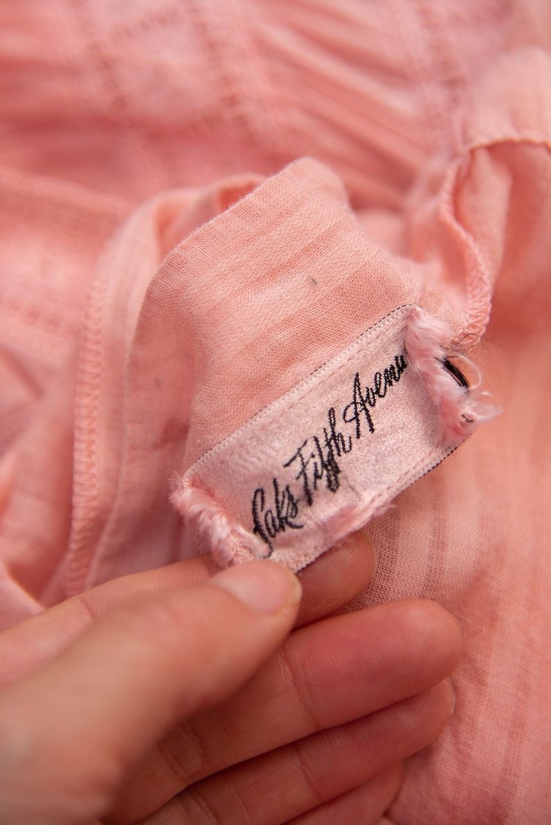 May include: A close-up of a pink fabric garment tag with black text that reads "Saks Fifth Avenue".