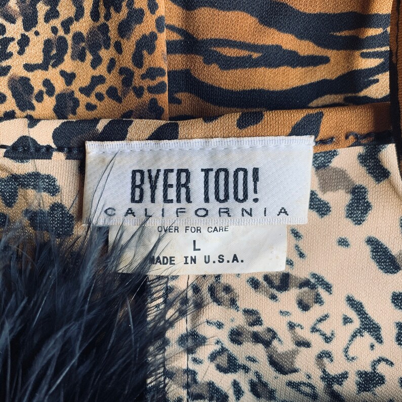 May include: A white tag with black text that reads "Byer Too! California" and "Over for Care" with a size "L" and "Made in U.S.A." The tag is attached to a brown and black leopard print fabric.