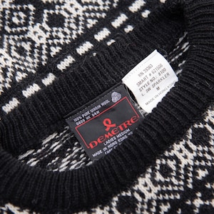 K&ouml;nnte beinhalten: Schwarz-wei&szlig;er Pullover mit Muster und einem schwarzen Etikett mit der Aufschrift "100% Pure Virgin Wool 0609 HK 84W" und einem roten Etikett mit der Aufschrift "Demetre Ladies Medium Made in Hong Kong  Care of"  RN 39363 SMART #621508 STYLE NO.: 8100 L. SW SPARKLER M MADE IN HONG KONG