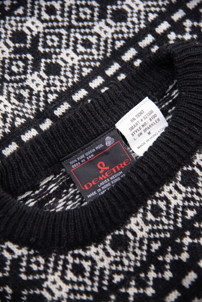 K&ouml;nnte beinhalten: Schwarz-wei&szlig;er Pullover mit Muster und einem schwarzen Etikett mit der Aufschrift "100% Pure Virgin Wool 0609 HK 84W" und einem roten Etikett mit der Aufschrift "Demetre Ladies Medium Made in Hong Kong  Care of"  RN 39363 SMART #621508 STYLE NO.: 8100 L. SW SPARKLER M MADE IN HONG KONG