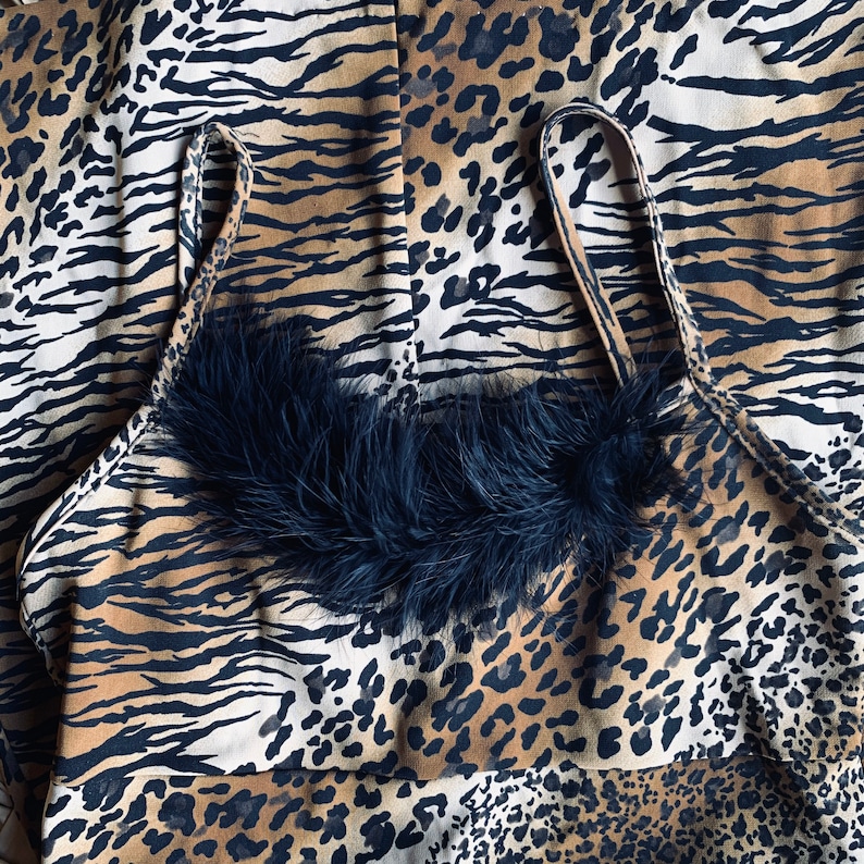 May include: A black and brown animal print halter top with a black feather trim. The top has a halter style with adjustable straps.