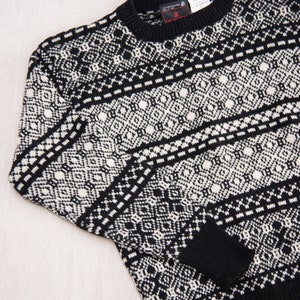 K&ouml;nnte beinhalten: Schwarz-wei&szlig;er Pullover mit Muster und Rundhalsausschnitt. Der Pullover hat ein kleines rotes Etikett mit dem Wort "Deutch" darauf.