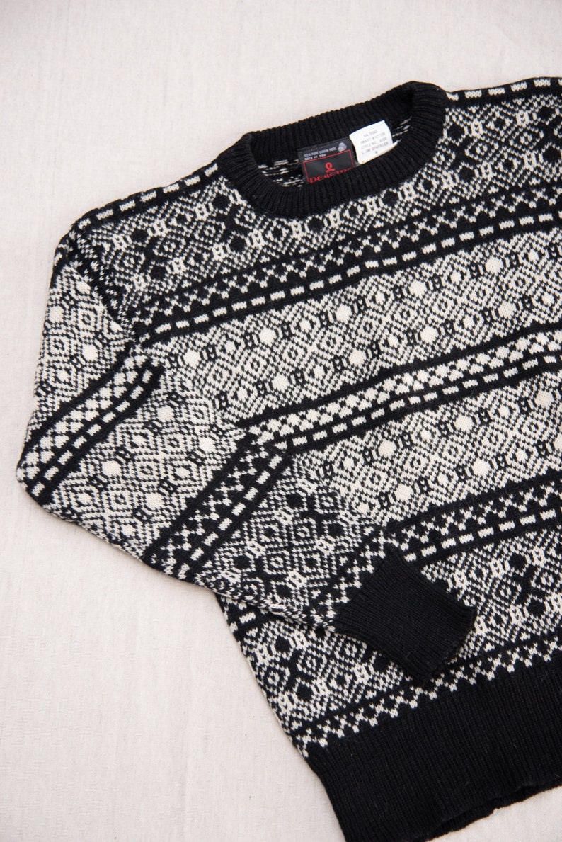 K&ouml;nnte beinhalten: Schwarz-wei&szlig;er Pullover mit Muster und Rundhalsausschnitt. Der Pullover hat ein kleines rotes Etikett mit dem Wort "Deutch" darauf.