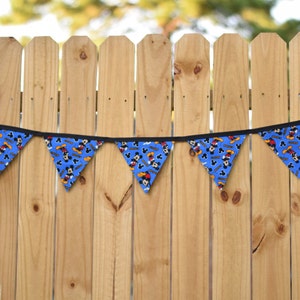 May include: A blue and yellow Mickey Mouse themed banner with black trim hangs against a wooden fence.