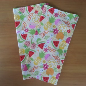 May include: Two yellow fabric tea towels with a colorful fruit pattern. The pattern includes watermelon, pineapple, lemons, limes, and strawberries.
