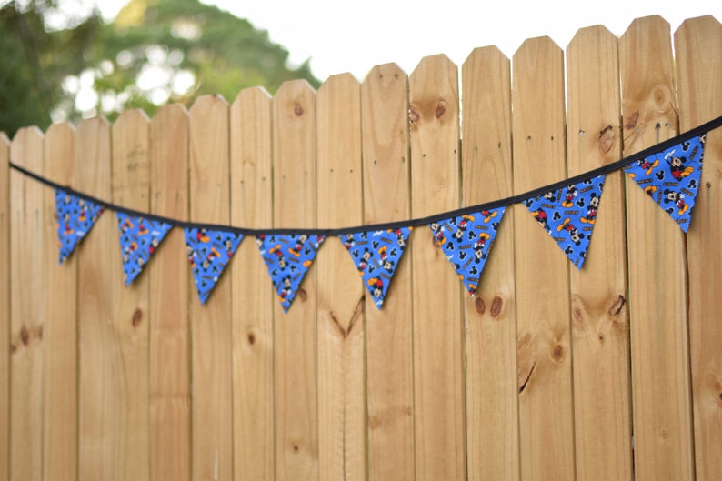 May include: A blue and black bunting with a Mickey Mouse pattern hangs on a wooden fence.