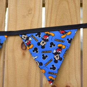 May include: A blue and black bunting with a Mickey Mouse pattern. The bunting has the word "Mickey" printed on each flag.