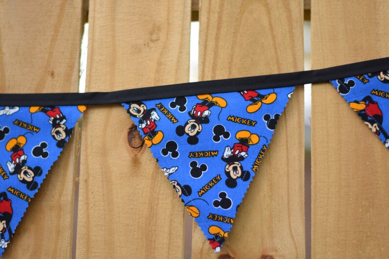 May include: A blue and black bunting with a Mickey Mouse pattern. The bunting has the word "Mickey" printed on each flag.