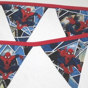May include: A fabric bunting banner featuring triangular flags with a repeating Spider-Man graphic. Each flag displays the character in a red and blue suit against a blue geometric city background, all connected by a solid red fabric ribbon trim.