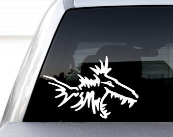 May include: A white vinyl sticker of a stylized sea monster with sharp teeth and fins, applied to the back window of a silver pickup truck.