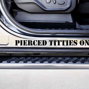 May include: A close-up of a black truck step with the words "Pierced Titties Only" printed in black stencil letters.