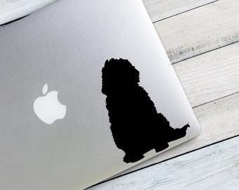 May include: A black silhouette of a small dog sitting on a silver laptop. The dog is facing to the right and has a fluffy tail.