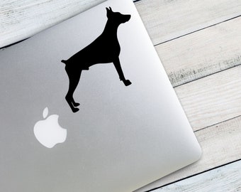 May include: A black silhouette of a Doberman Pinscher dog sticker on a silver laptop.