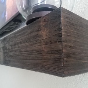 May include: A dark brown wooden shelf with a rough, textured surface. The shelf is mounted to a white wall and appears to be made from reclaimed wood.