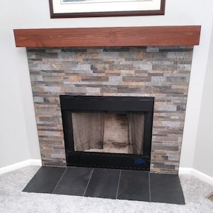 May include: A fireplace with a wood mantel and a stone surround. The fireplace has a black metal firebox with a screen.