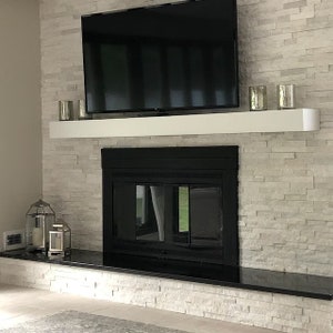 May include: A black fireplace with a white mantel and a black television on top. The fireplace is surrounded by white stone tiles.