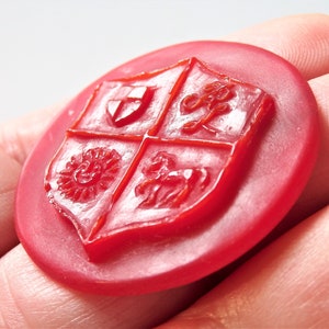 May include: A red wax seal with a raised design of a shield divided into four sections. Each section features a different symbol: a cross, a flower, a sun, and a horse.