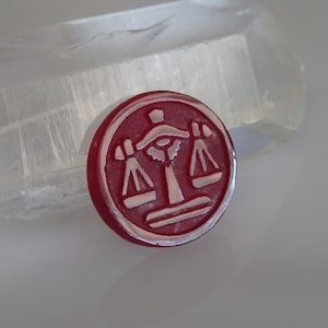 May include: A red wax seal with a white image of a scale, symbolizing justice.