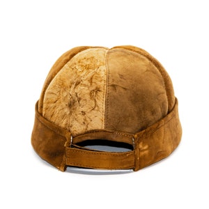 May include: A brown suede and fur baseball cap with a curved brim and a strap in the back.