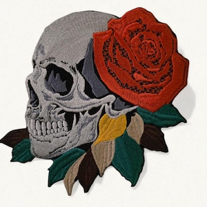 May include: Embroidered patch depicting a grey skull with a large red rose. The rose is positioned behind the skull, with green, yellow, and brown leaves at the base. Ideal for customising clothing or accessories, this patch is a striking design.
