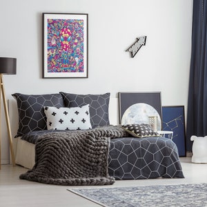 Puede incluir: Un edred&oacute;n con estampado geom&eacute;trico en blanco y negro con una manta de punto gris encima. La cama tiene dos almohadas con estampado geom&eacute;trico en blanco y negro y una almohada blanca con cruces negras. Hay una impresi&oacute;n enmarcada de un personaje de dibujos animados de colores sobre la cama.