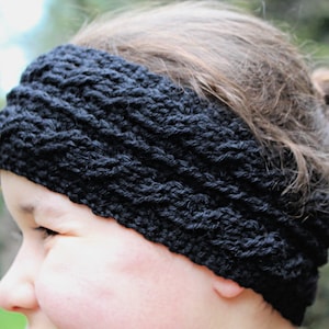 Könnte beinhalten: Ein schwarzes Strick Stirnband mit einem strukturierten Muster. Das Stirnband wird von einer Person mit braunen Haaren getragen.