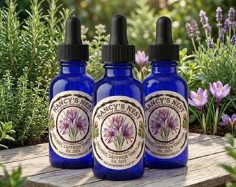 Może przedstawiać: Trzy kobaltowe szklane butelki z zakraplaczami i czarnymi nakrętkami, każda z kremową etykietą z napisem Nancy's Nest, Nurtured through Nature, Organic Saffron Tincture, Small-Batch Made, Est. 2023 oraz nancysnestidaho.etsy.com.