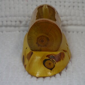 May include: A wooden log-shaped business card holder with a natural wood finish. The holder is made from a single piece of wood and has a unique grain pattern. It is sitting on a white surface.