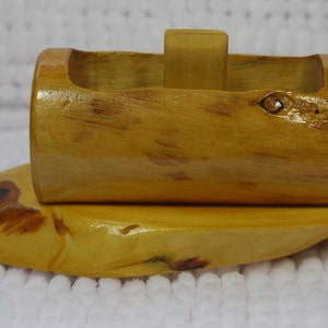 May include: A wooden boat toy with a natural wood finish. The boat has a rounded hull and a small, rectangular sail. The boat is sitting on a white surface.