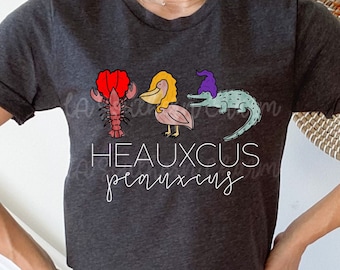 May include: Dark gray heather t-shirt with a graphic of a lobster, pelican, and alligator wearing a purple hat. The text "HEAUXCUS  peauxcus" is printed on the shirt.
