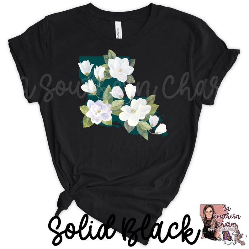 K&ouml;nnte beinhalten: Schwarzes T-Shirt mit einem wei&szlig;en Magnolienbl&uuml;ten-Design in Form des Bundesstaates Louisiana. Das Design ist auf einem blaugr&uuml;nen Hintergrund.