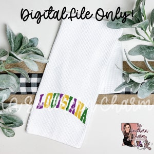 May include: White kitchen towel with the word "LOUISIANA" in a purple, yellow, and green arch. The towel is folded in half and has a waffle texture.