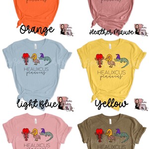 May include: Six different colored t-shirts with a graphic of a crawfish, pelican, and alligator with the text "HEAUXCUS peauxcus". The t-shirt colors are orange, heather mauve, light blue, yellow, pink, and heather olive.