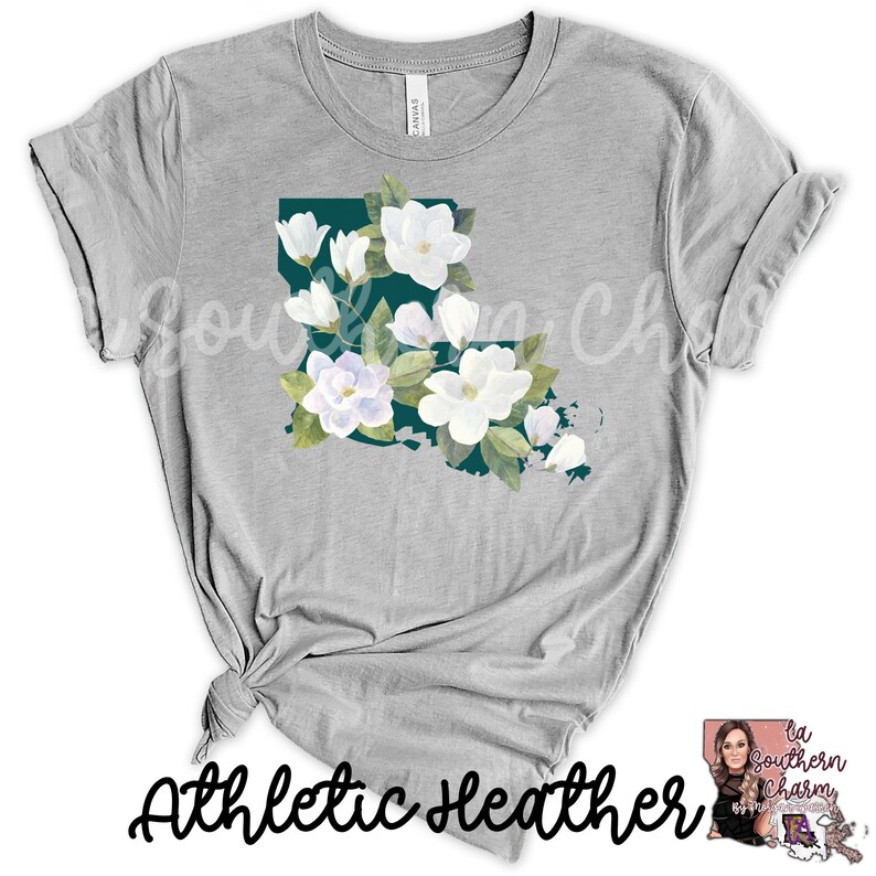 K&ouml;nnte beinhalten: Ein graues T-Shirt mit einer t&uuml;rkisfarbenen Umrandung des Bundesstaates Louisiana, verziert mit wei&szlig;en Magnolienbl&uuml;ten. Der Text "Athletic Heather" ist unten auf dem T-Shirt aufgedruckt.