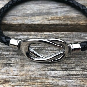 May include: A black leather bracelet with a silver knot clasp.
