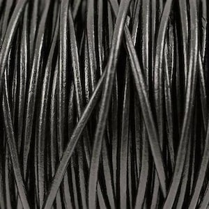 May include: Close-up of a spool of black leather cord. The cord is tightly wound and has a smooth, glossy finish.