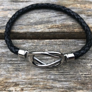 May include: A black leather bracelet with a silver knot clasp.