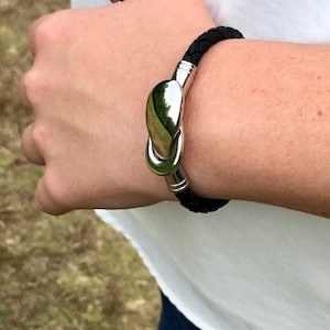 May include: A black leather bracelet with a silver clasp. The clasp is shaped like a teardrop and has a smooth, polished finish.