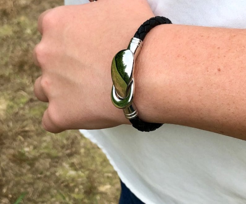 May include: A black leather bracelet with a silver clasp. The clasp is shaped like a teardrop and has a smooth, polished finish.