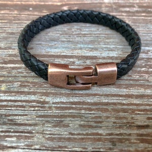 Peut inclure: Un bracelet en cuir tress&eacute; noir avec une fermeture en cuivre.
