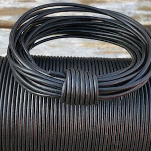 May include: A spool of black leather cord, tightly wound and displayed. A portion of the cord is looped and knotted, showcasing its flexibility. The cord appears to be approximately 2mm in diameter, suitable for various crafting projects.