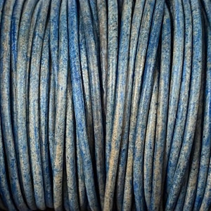 Op de afbeelding: Close-up van een spoel met blauwe en beige lederen koord. Het koord is strak gewikkeld en heeft een textuur.