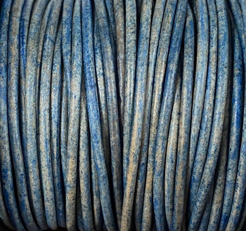 Op de afbeelding: Close-up van een spoel met blauwe en beige lederen koord. Het koord is strak gewikkeld en heeft een textuur.